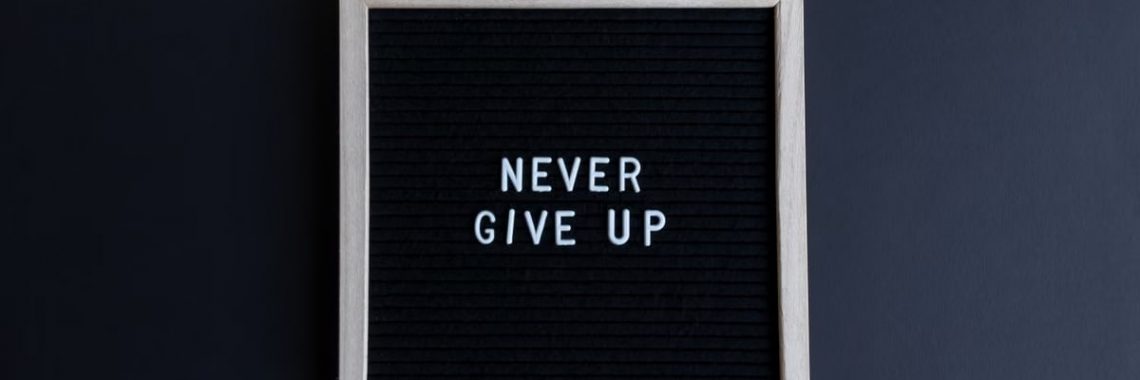 Inspirational letter board with 'Never Give Up' phrase on gray background.